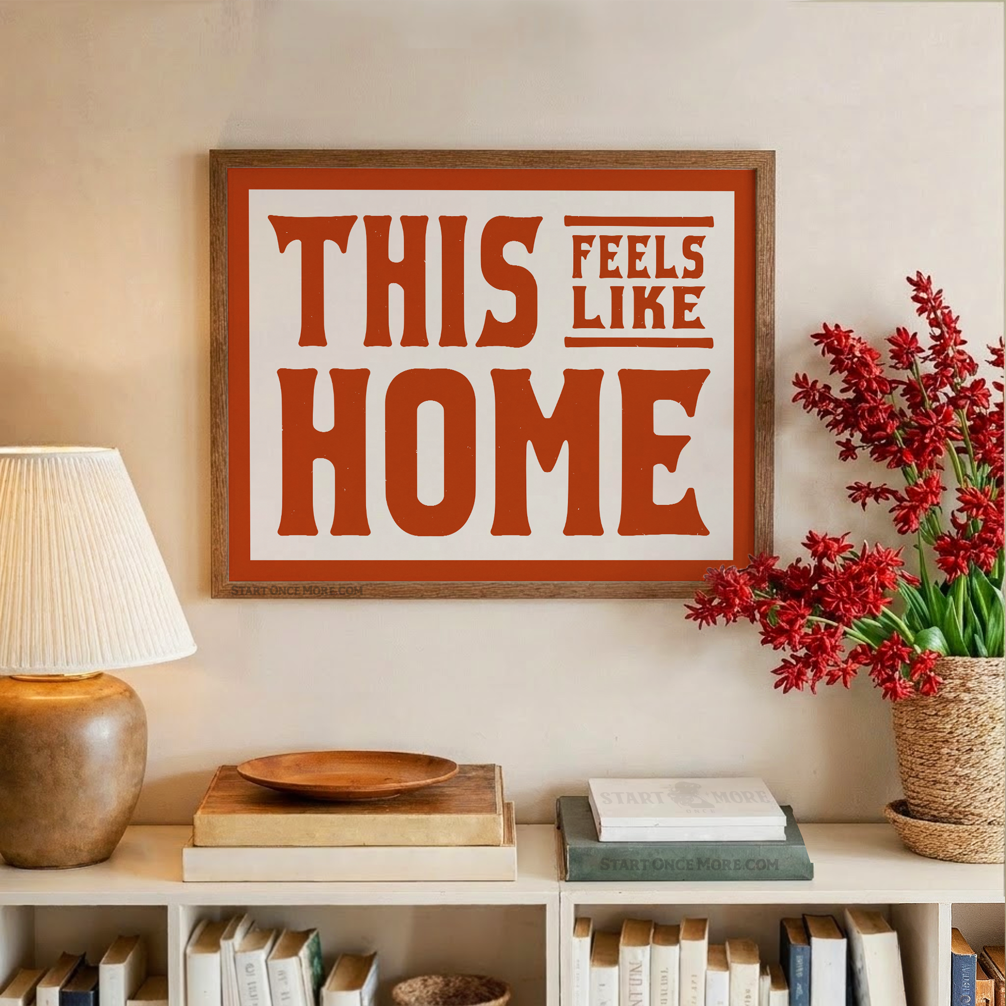 Framed artwork with 'This Feels Like Home' text on a wall above a shelf with books and decor.